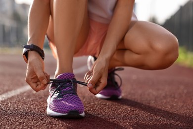 Photo of Woman tying shoelace of sneaker at stadium, closeup