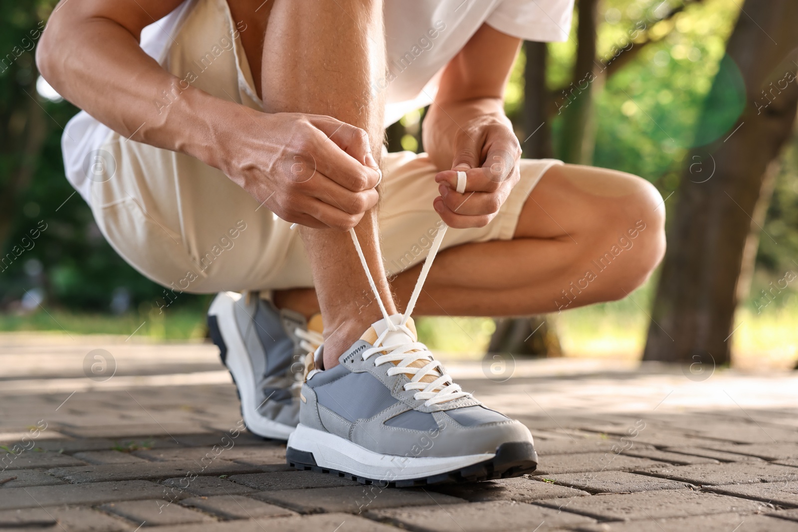 Photo of Man tying shoelace of grey sneaker outdoors, closeup