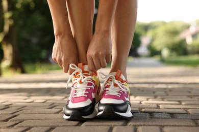 Photo of Woman tying shoelace of sneaker outdoors, closeup