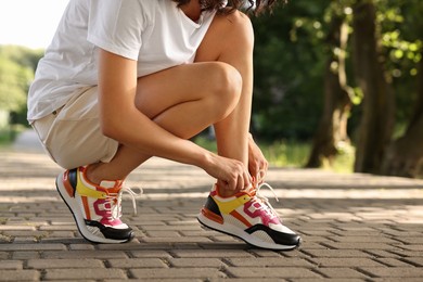 Woman tying shoelace of sneaker outdoors, closeup. Space for text