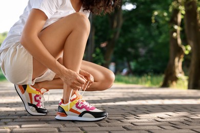 Photo of Woman tying shoelace of sneaker outdoors, closeup. Space for text