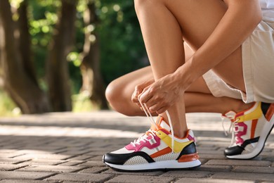 Photo of Woman tying shoelace of sneaker outdoors, closeup. Space for text