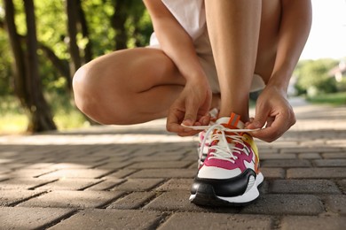 Woman tying shoelace of sneaker outdoors, closeup