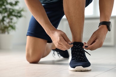 Photo of Man tying shoelace of sneaker indoors, closeup