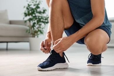 Photo of Man tying shoelace of sneaker indoors, closeup. Space for text