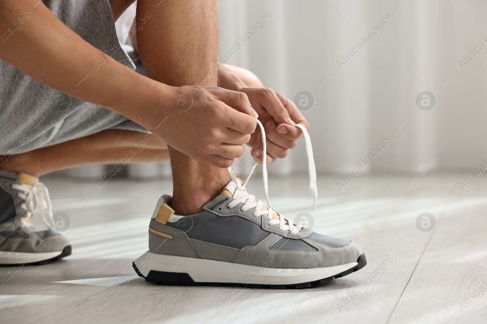 Photo of Man tying shoelace of sneaker indoors, closeup