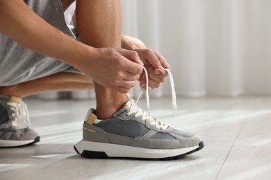 Photo of Man tying shoelace of sneaker indoors, closeup