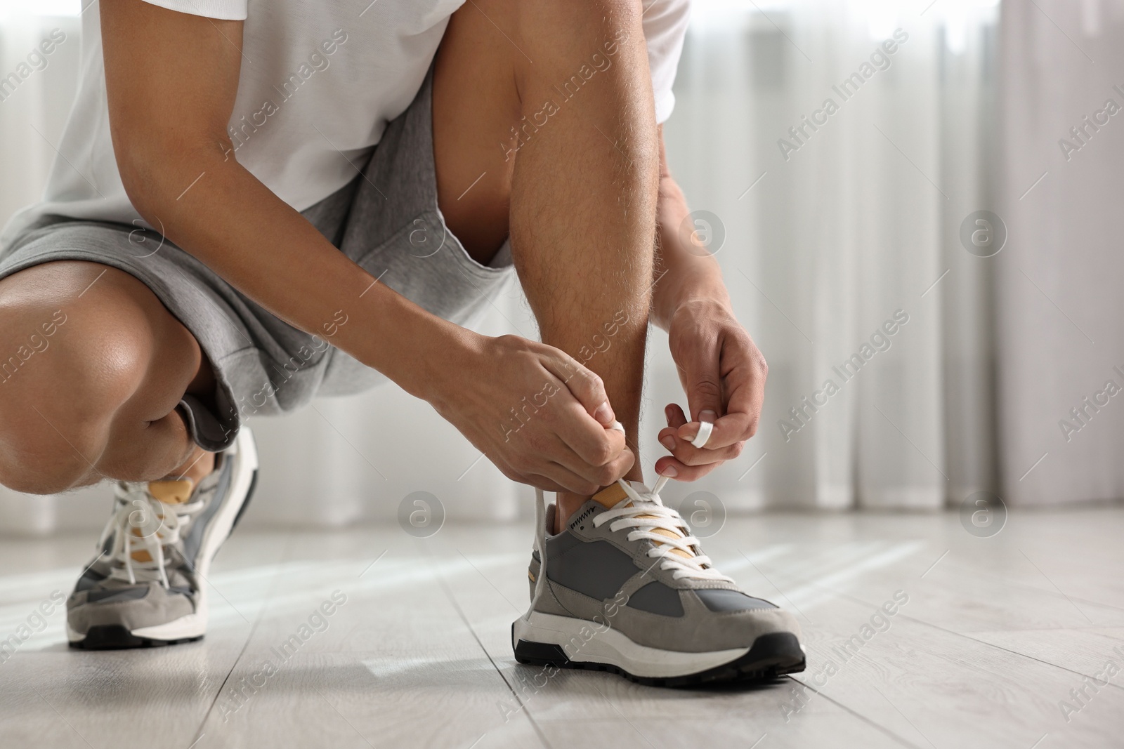 Photo of Man tying shoelace of sneaker indoors, closeup. Space for text