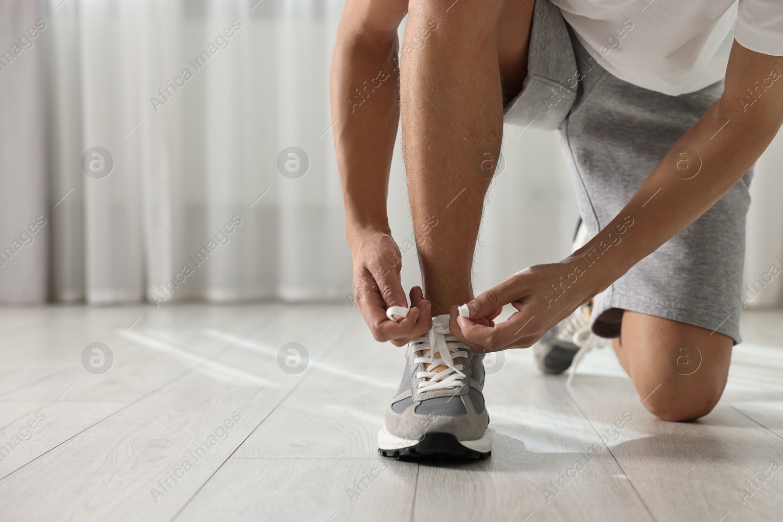 Photo of Man tying shoelace of sneaker indoors, closeup. Space for text