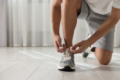 Man tying shoelace of sneaker indoors, closeup. Space for text