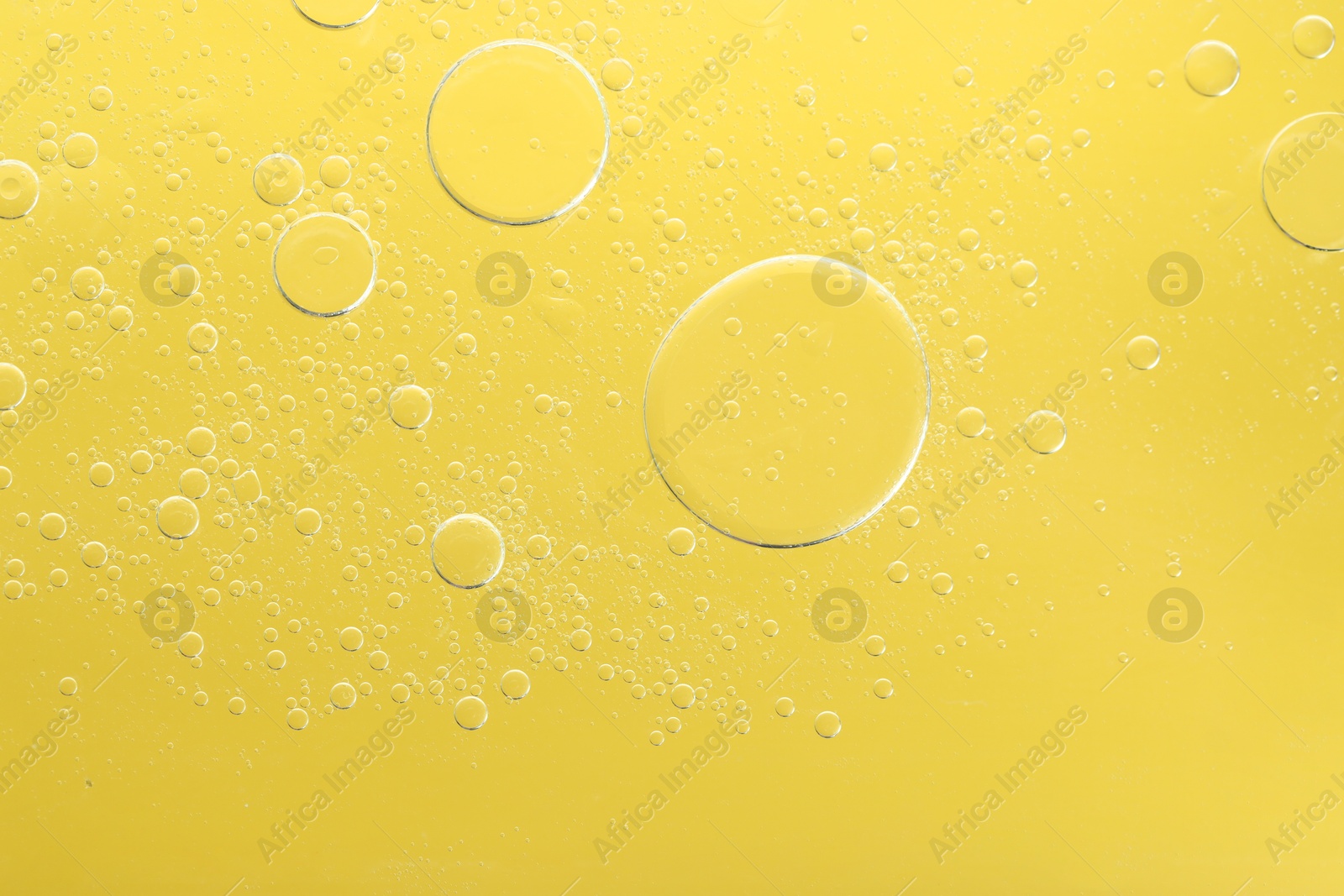 Photo of Essential oil bubbles on yellow background, macro view. Cosmetic product