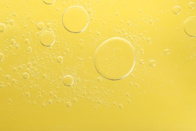 Photo of Essential oil bubbles on yellow background, macro view. Cosmetic product