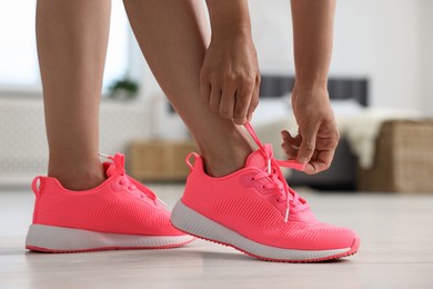 Photo of Woman tying shoelace of pink sneaker indoors, closeup