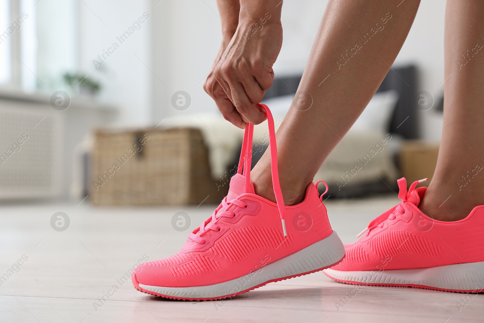 Photo of Woman tying shoelace of pink sneaker indoors, closeup. Space for text