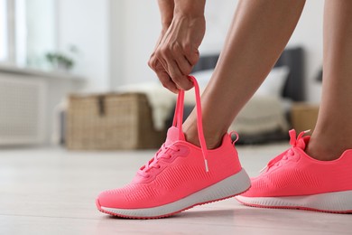 Photo of Woman tying shoelace of pink sneaker indoors, closeup. Space for text