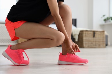 Photo of Woman tying shoelace of pink sneaker indoors, closeup. Space for text