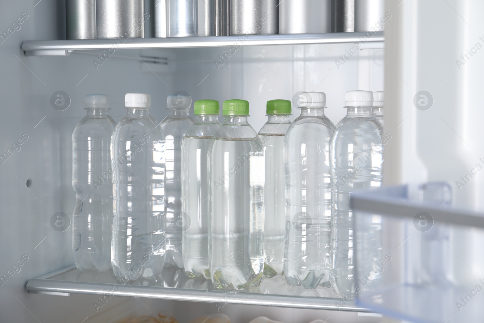 Photo of Cans of beer and water bottles in refrigerator, closeup