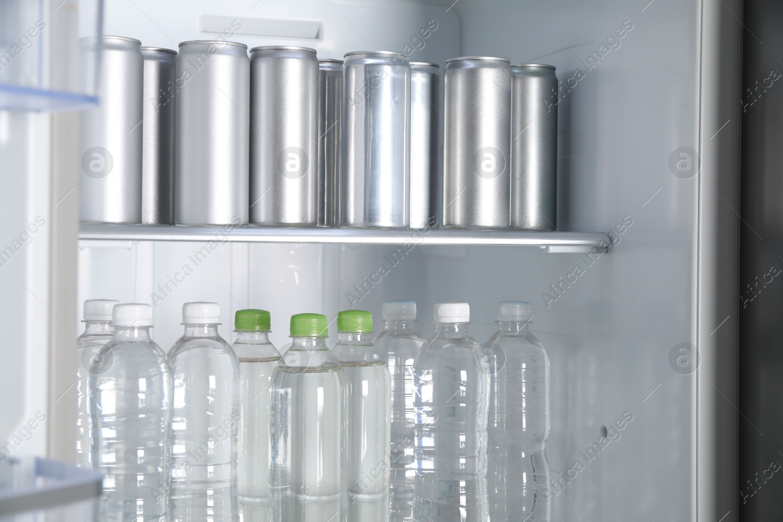 Photo of Cans of beer and water bottles in refrigerator, closeup