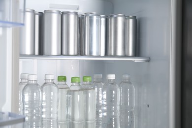 Cans of beer and water bottles in refrigerator, closeup