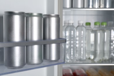 Cans of beer and water bottles in refrigerator, closeup