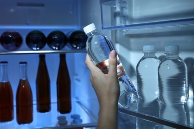 Woman taking bottle of water from refrigerator, closeup