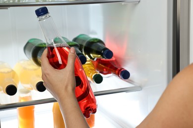 Woman taking bottle with drink from refrigerator, closeup