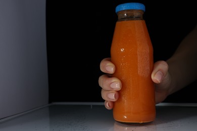 Woman taking bottle of juice from refrigerator, closeup. Space for text