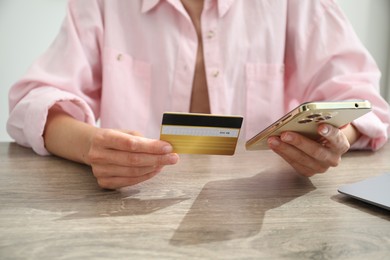 Photo of Woman with credit card using smartphone at wooden table indoors, closeup