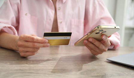 Photo of Woman with credit card using smartphone at wooden table indoors, closeup