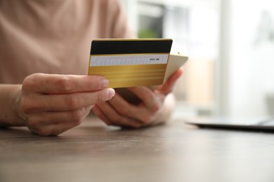 Photo of Woman with credit card using smartphone at wooden table indoors, closeup