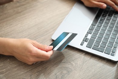 Photo of Woman with credit card using laptop at wooden table indoors, closeup