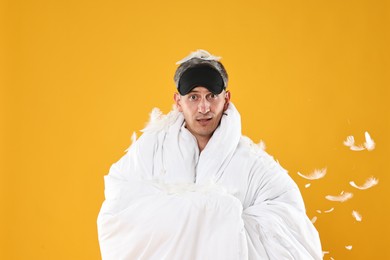 Photo of Overslept man with sleep mask wrapped in blanket on orange background