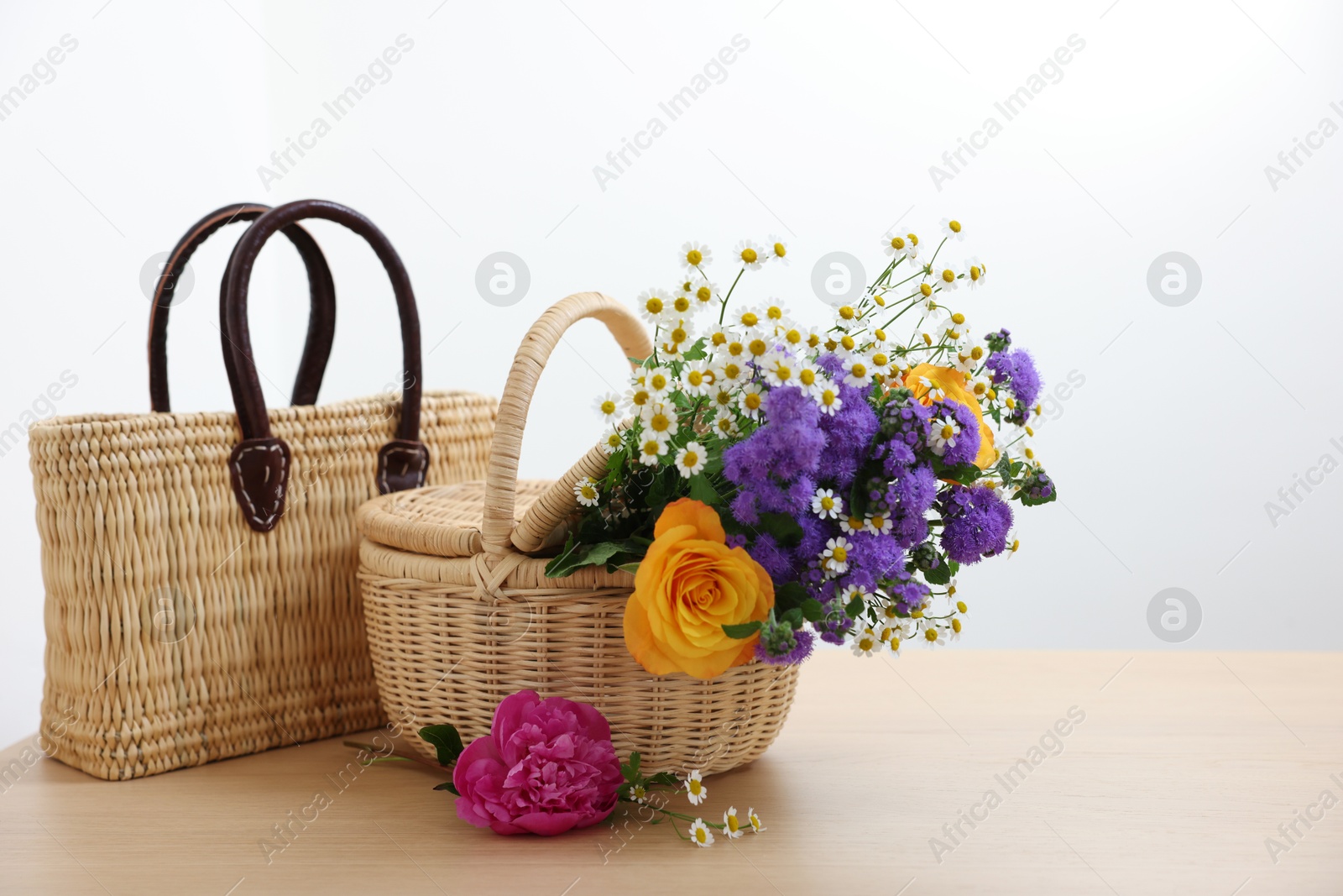 Photo of Wicker baskets and beautiful flowers on light wooden table, space for text