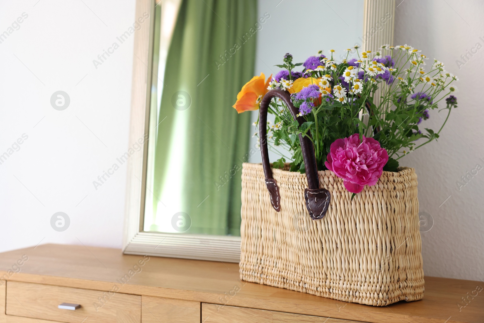 Photo of Wicker basket with beautiful flowers on wooden table indoors, space for text