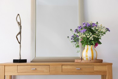 Beautiful flowers in vase and mirror on wooden table indoors