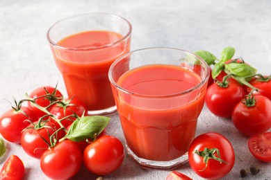 Photo of Tasty tomato juice in glasses, basil leaves and fresh vegetables on light grey table