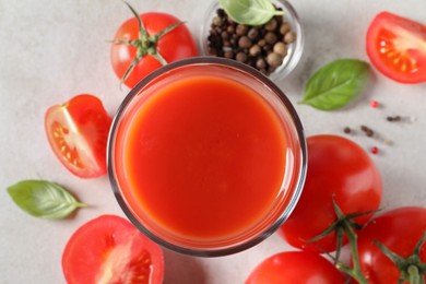 Photo of Tasty tomato juice in glass, basil leaves, peppercorns and fresh vegetables on light grey table, flat lay