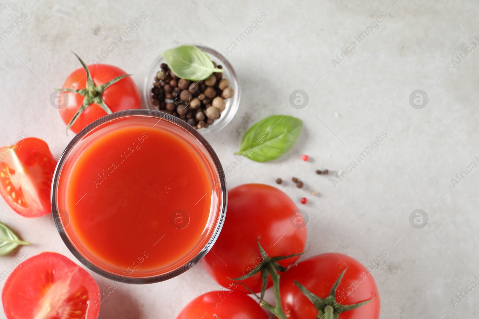 Photo of Tasty tomato juice in glass, basil leaves, peppercorns and fresh vegetables on light grey table, flat lay. Space for text