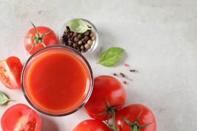 Tasty tomato juice in glass, basil leaves, peppercorns and fresh vegetables on light grey table, flat lay. Space for text