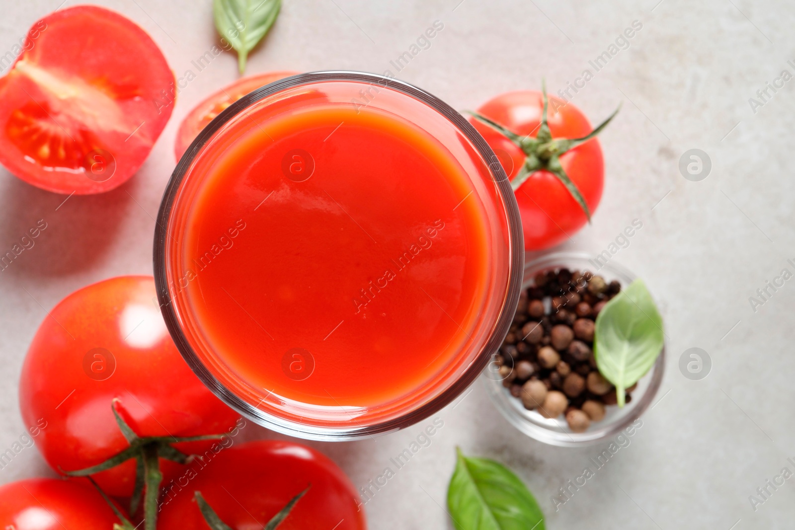 Photo of Tasty tomato juice in glass, basil leaves, peppercorns and fresh vegetables on light grey table, flat lay