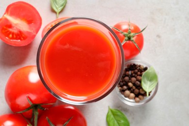 Photo of Tasty tomato juice in glass, basil leaves, peppercorns and fresh vegetables on light grey table, flat lay