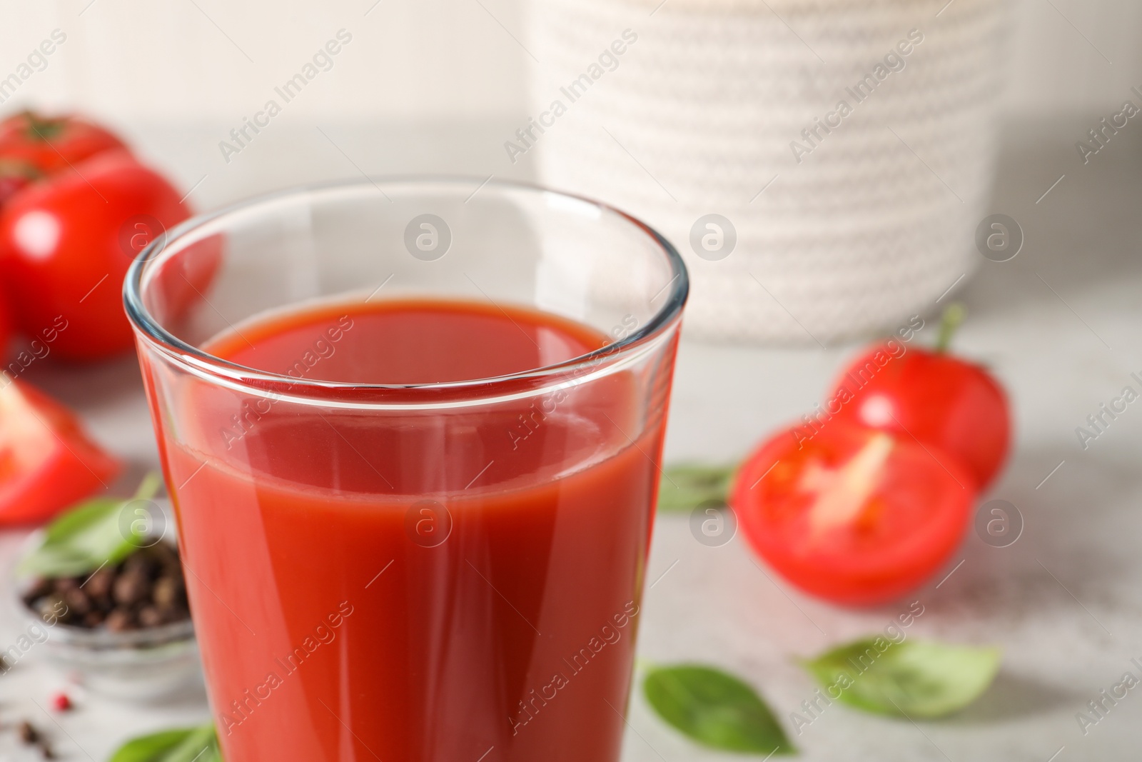 Photo of Tasty tomato juice in glass, basil leaves and fresh vegetables on table, closeup