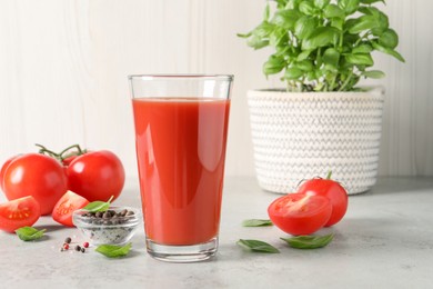 Tasty tomato juice in glass, basil leaves, peppercorns and fresh vegetables on light grey table