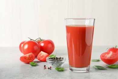 Photo of Tasty tomato juice in glass, basil leaves, peppercorns and fresh vegetables on light grey table