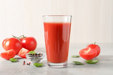 Photo of Tasty tomato juice in glass, basil leaves, peppercorns and fresh vegetables on light grey table