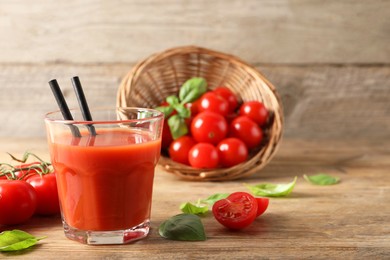 Photo of Tasty tomato juice in glass, basil leaves and fresh vegetables on wooden table