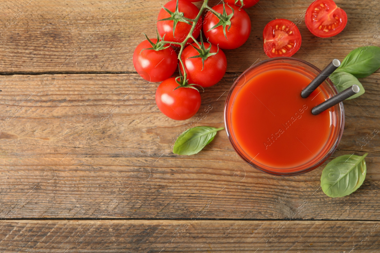 Photo of Tasty tomato juice in glass, basil leaves and fresh vegetables on wooden table, flat lay. Space for text