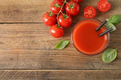 Photo of Tasty tomato juice in glass, basil leaves and fresh vegetables on wooden table, flat lay. Space for text