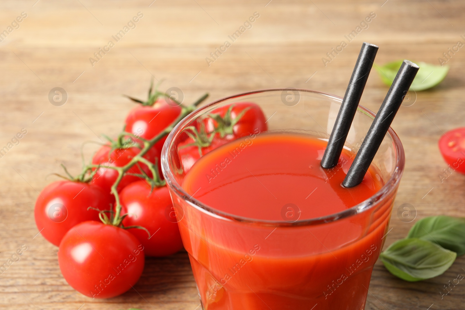 Photo of Tasty tomato juice in glass, basil leaves and fresh vegetables on wooden table, closeup