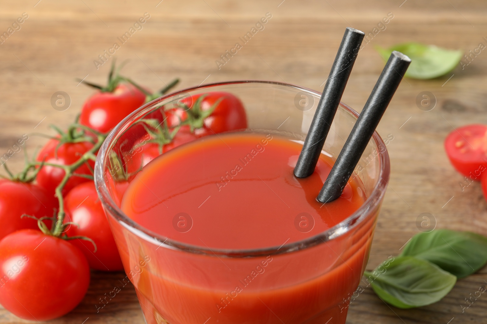 Photo of Tasty tomato juice in glass, basil leaves and fresh vegetables on wooden table, closeup